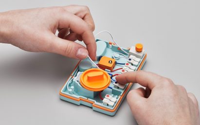 Photo of the inside of the Ambessa Play flashlight, showing colourful, keyboard key-like cable connectors along the right side and white, blue and red wires connecting them. A person's hands are playing with the wires