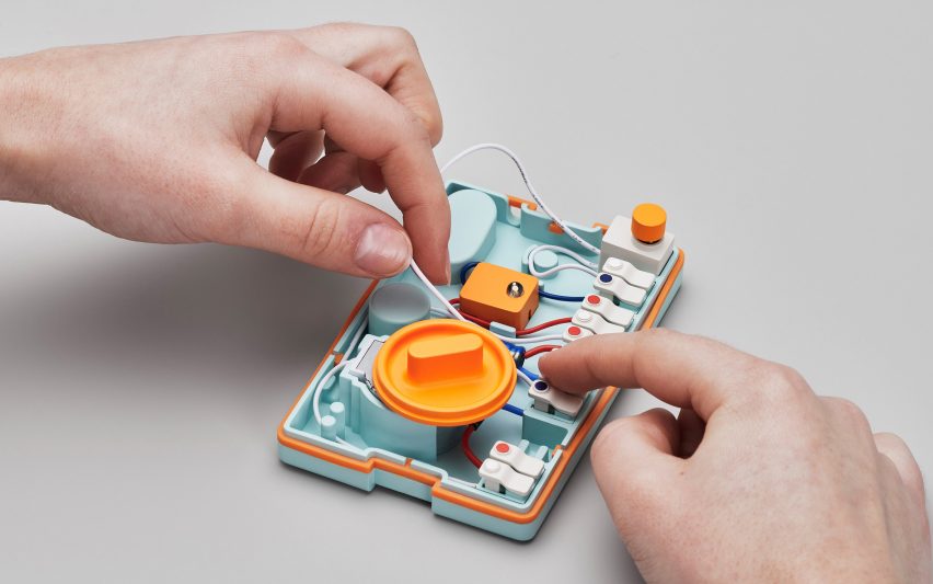 Photo of the inside of the Ambessa Play flashlight, showing colourful, keyboard key-like cable connectors along the right side and white, blue and red wires connecting them. A person's hands are playing with the wires