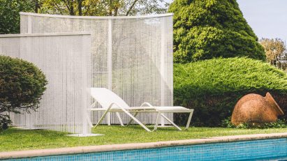 White lounger beside pool between white chain curtains
