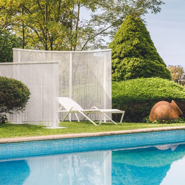 White lounger beside pool between white chain curtains