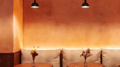 Restaurant interior with an orange ombre wall, black pendant lights, bench seating and wooden tables and chairs