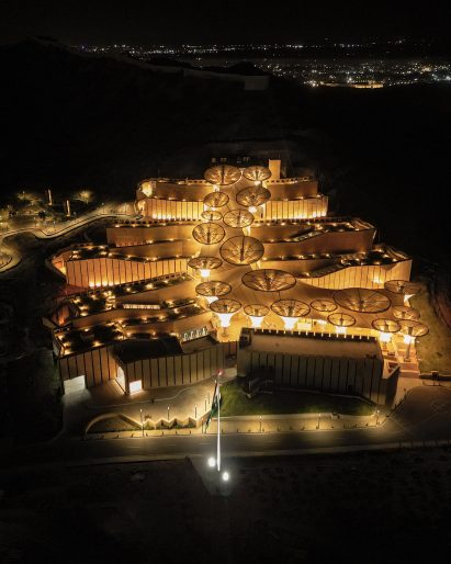 Exterior of the Smritivan Earthquake Memorial Museum by Vastushilpa Constultants with stone walls zigzagging up a sloped site lit up at night
