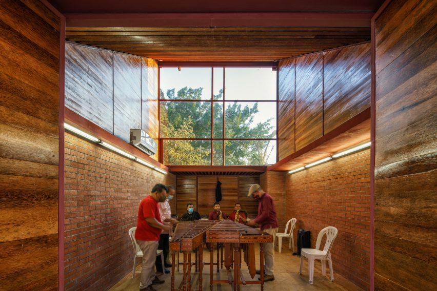 Internal wood-clad space with people around a table and a large high window