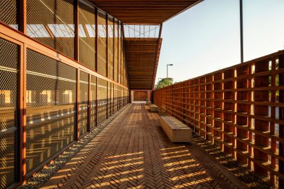 A covered exterior walkway with a brick floor and timber walls next to a glazed gable-ended building