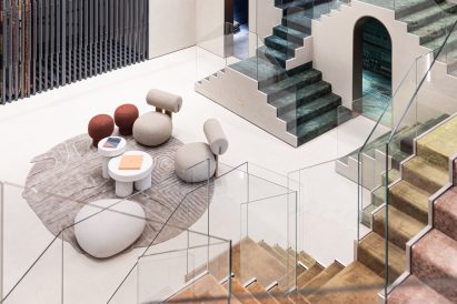 Photo looking down on an arrangement of playful, round furniture on a circular rug, all in neutral colours but surrounded by staircases carpeted in a rainbow of jewel tones