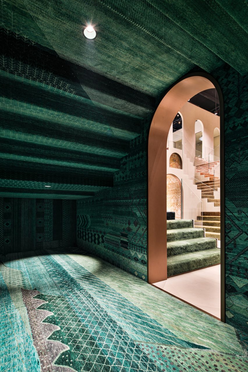 Photo of the Emerald Room at the Jaipur Rugs Dubai showroom showing floor-to-ceiling emerald green, intricately patterned rugs and an arched doorway framing the store beyond