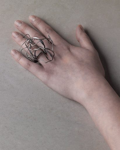 Photograph of a hand wearing a silver ring with an oversized swirling structure
