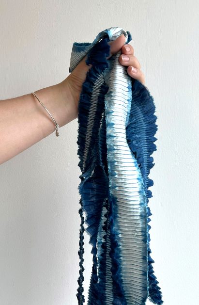 Hand holding blue and silver fabric in front of white wall