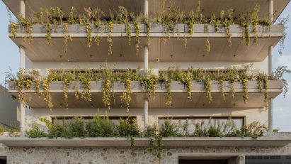 A four-storey apartment building in Mexico with a stone wall and planted balconies