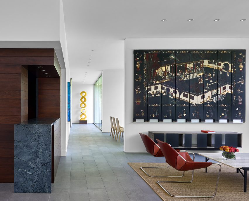 Dining space with white walls, porcelain floor tiles, dark wood wall cladding and red chairs