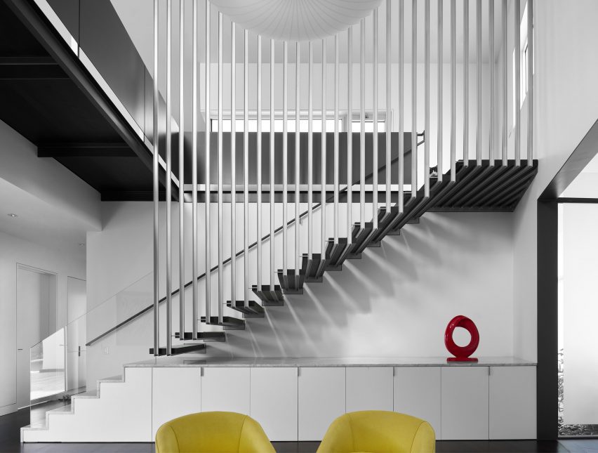 White double-height interior with a floating staircase and built-in cupboards