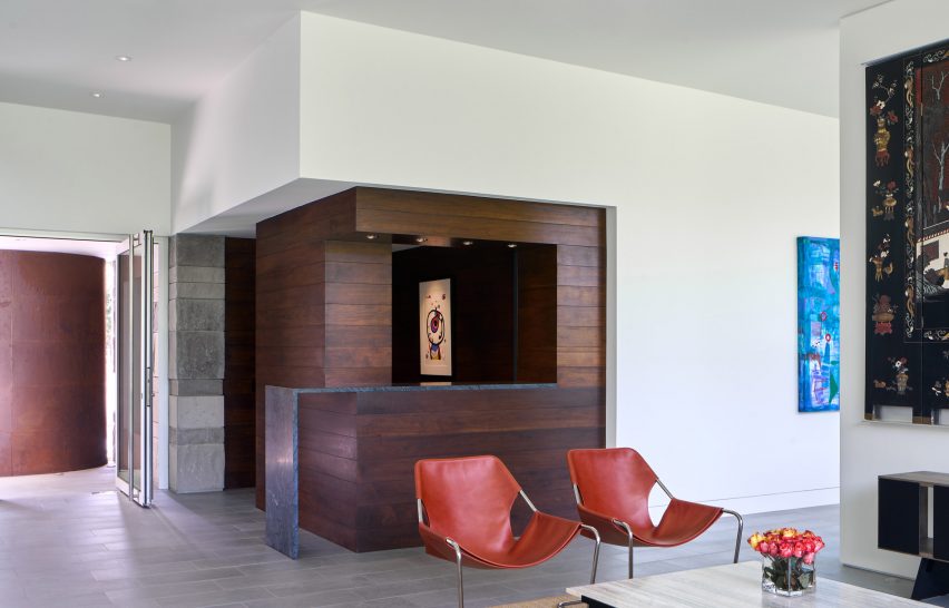 Lounge space with red chairs and a white corner wall with dark wood cut-out