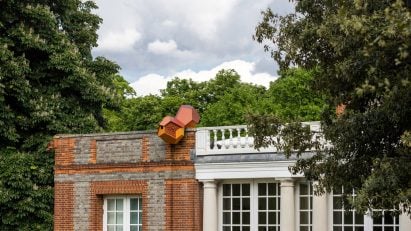 Photo of the outside of the Serpentine South building with a small, birdhouse-like Tomás Saraceno Cloud Cities sculpture sitting on the facade