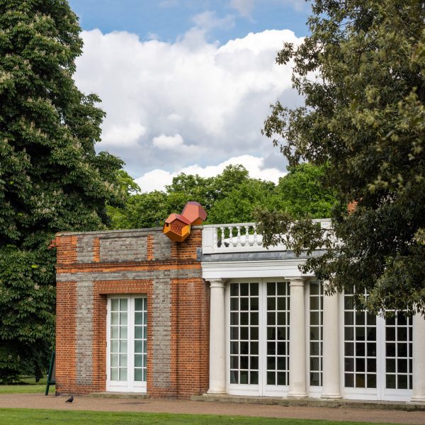 Photo of the outside of the Serpentine South building with a small, birdhouse-like Tomás Saraceno Cloud Cities sculpture sitting on the facade