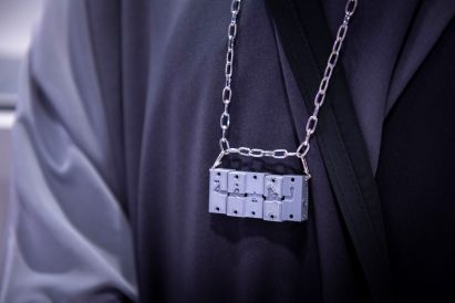 Five small engraved cubes on a silver chain worn by a person in black clothing