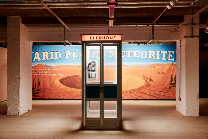 A telephone booth in front of a meteor crater billboard poster