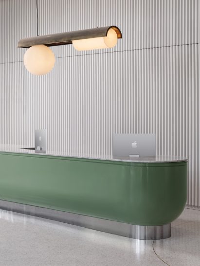 Rounded mint-green reception desk in front of white tambour wall