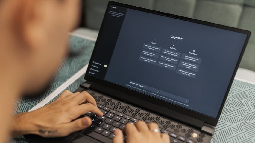 Photo of a person seen from behind over their shoulder using ChatGPT on their laptop