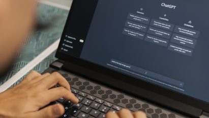 Photo of a person seen from behind over their shoulder using ChatGPT on their laptop