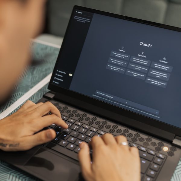 Photo of a person seen from behind over their shoulder using ChatGPT on their laptop