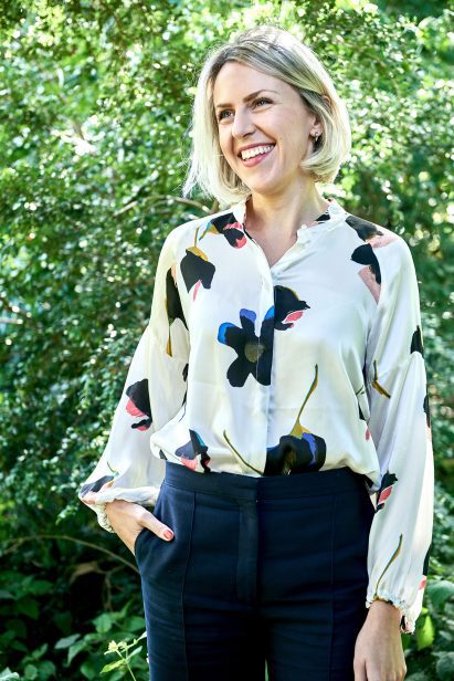 Photo of Alexandra Daisy Ginsberg, smiling and standing outdoors in a leafy green environment
