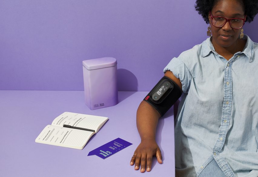 Photo of a Black woman with a blood pressure cuff on her right arm, which rests on a table. Spora Health's Momma's Kit tin also sits on the table, along with an open notebook with prompts printed on its pages