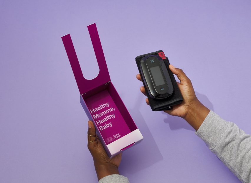 Photo of a person's hands removing a blood pressure cuff from a magenta-coloured box with text on the inside that reads 'healthy momma, healthy baby'