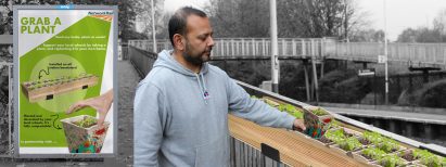 Man taking a potted plant from a train station banister with an information poster beside him