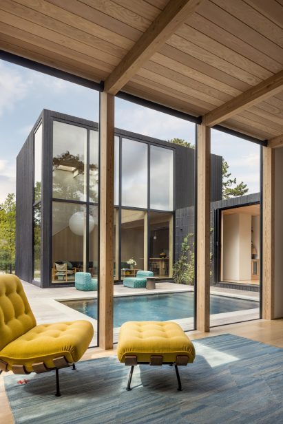 Minimalist house clad in blackened wood arranged around swimming pool