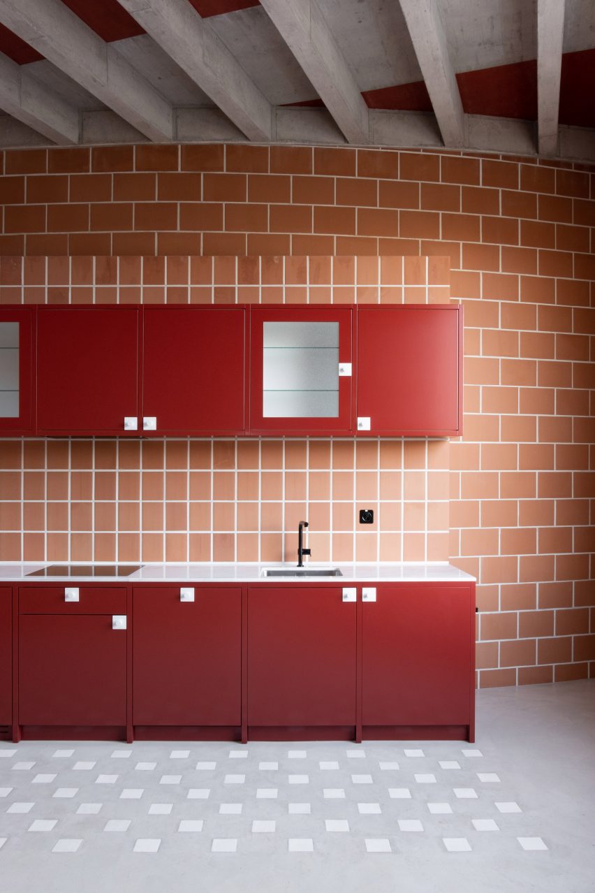 Red kitchen units in a workshop with terracotta brick walls and concrete floors and roof beams