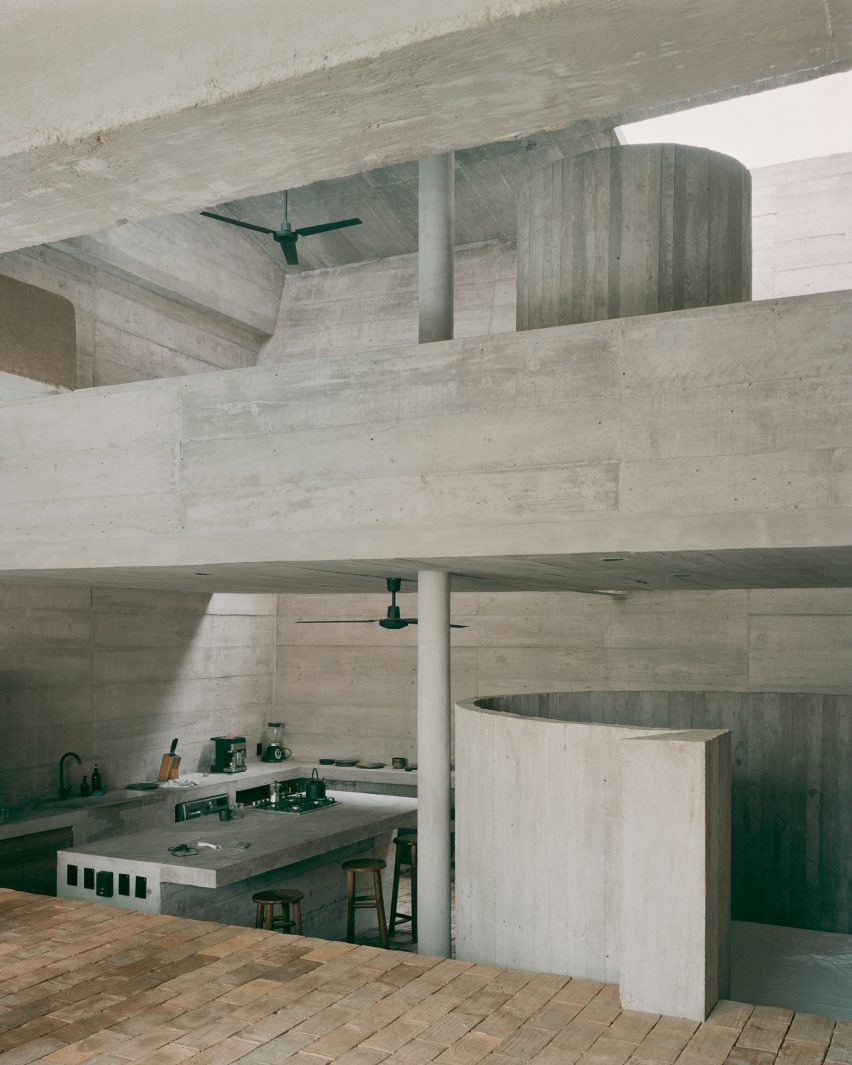 The interior of a concrete home that features a mezzanine and a below-ground kitchen