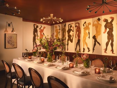 Long dining table laid for a party in front of a wall mural