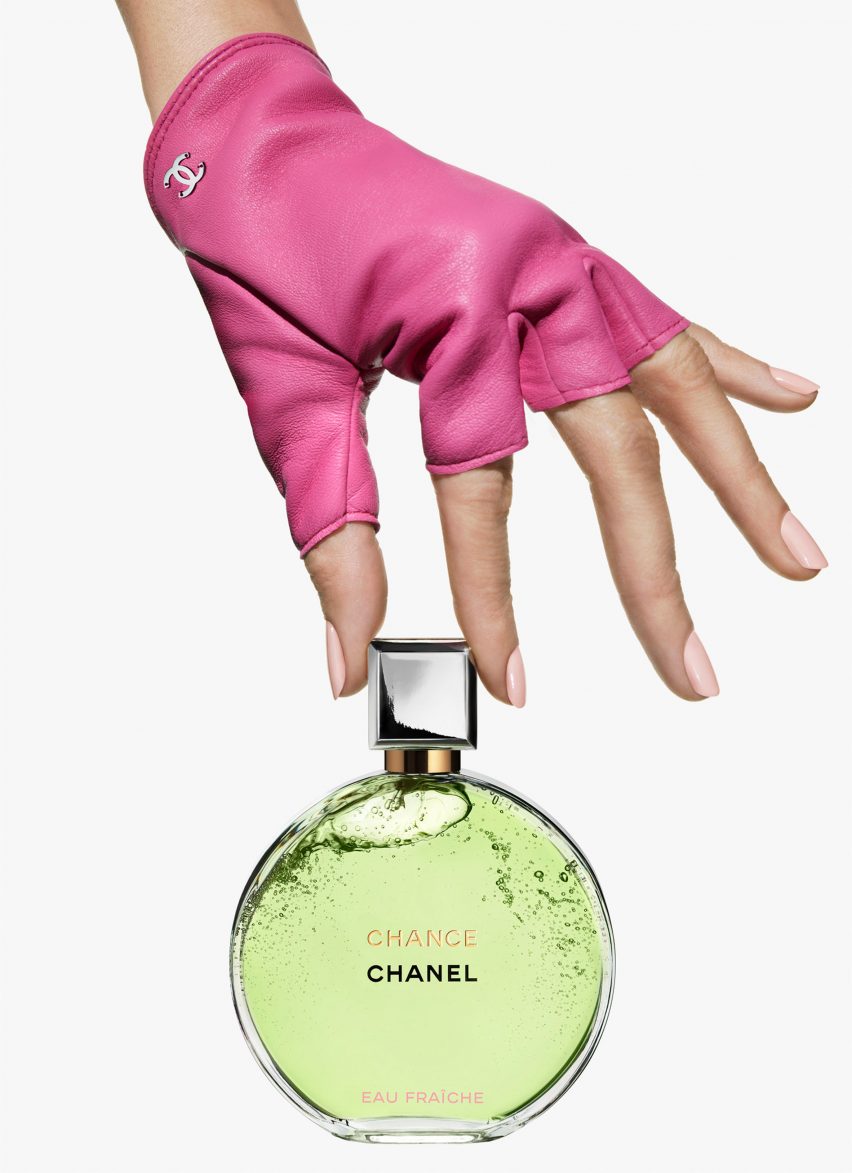 A pink-gloved hand holding a bottle of perfume in a round bottle