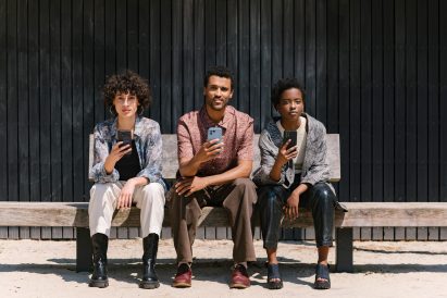 Photo of three young people sitting in a row holding Fairphone 5s in different colours. From left: transparent, blue then black