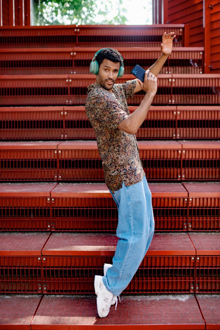 Photo of a man dancing in front of red steps while holding a smartphone and wearing headphones