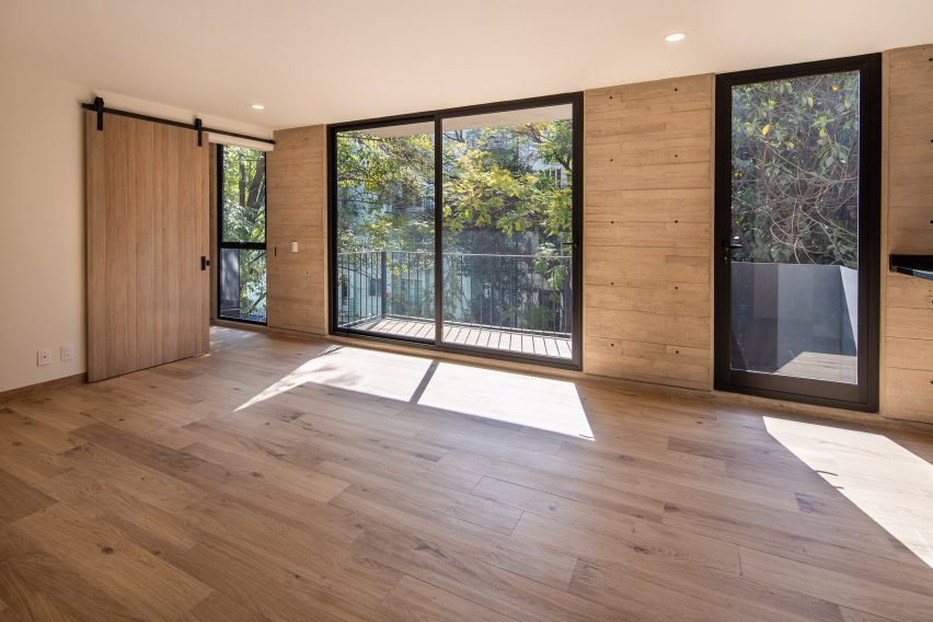 Interior space with board-formed concrete walls, wood flooring and glass doors leading to balconies