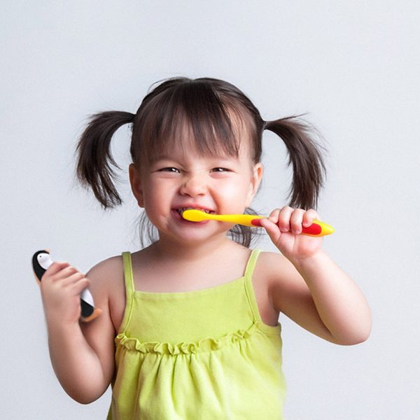 Young child brushing teeth and holding a penguin-shaped toothpaste dispenser