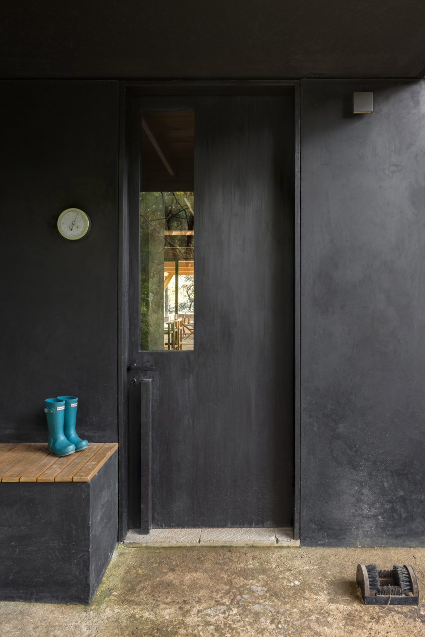 A black door with a bench next to it that has little blue rain boots