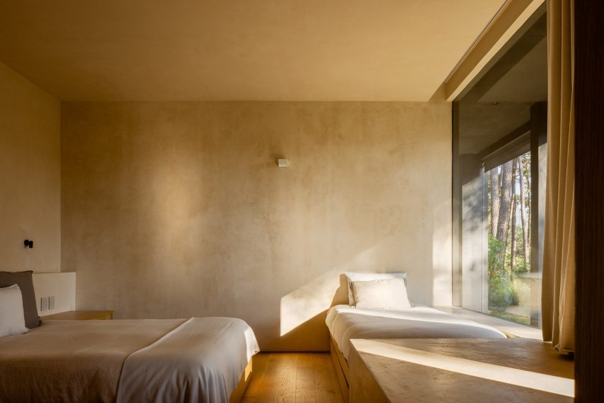 Two beds in a bedroom with light walls and a large window on one side