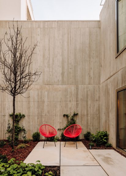 Residential courtyard in a concrete home with planting and red chairs