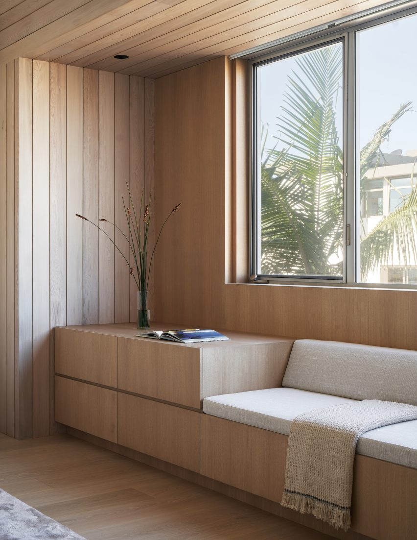 Built-in wooden seating with white upholstery below a window