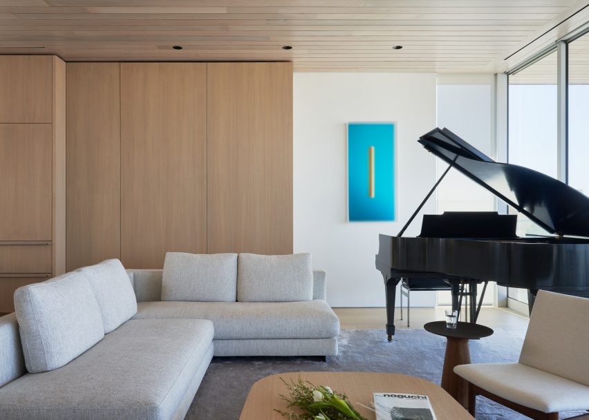 Living room with built-in wood storage, a grey sofa and a piano