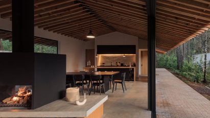 Open-plan living interior with stone floors, timber pitched roof and glazed walls leading outside