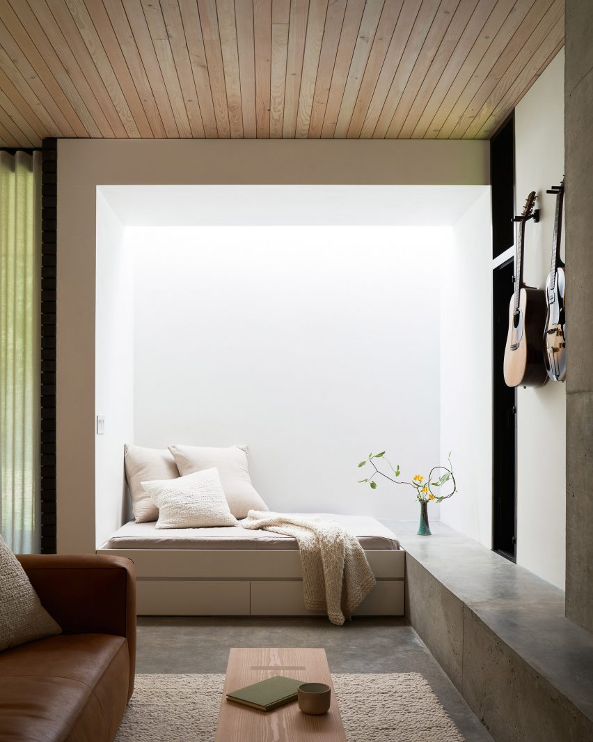 Concrete L-shaped bench in a white room with cushions and a blanket