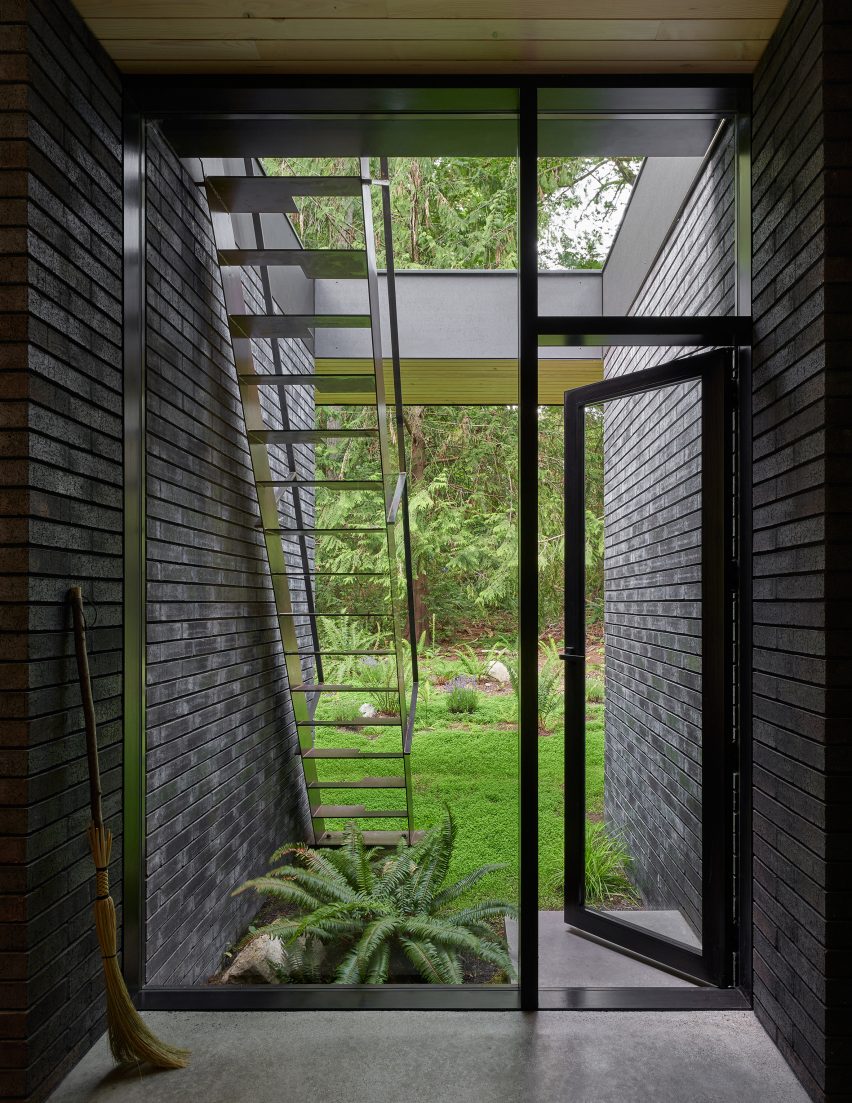 Room with floor-to-ceiling windows and black brick walls extending into a garden