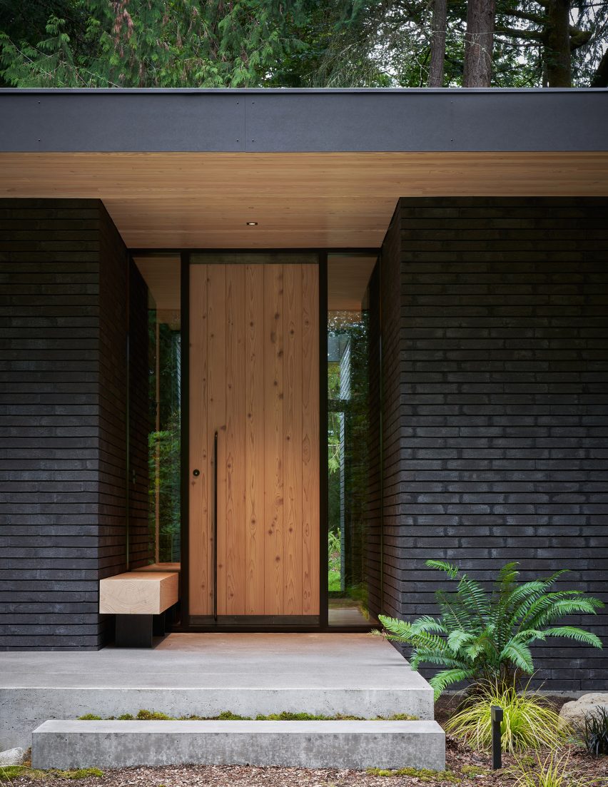 Wooden front door to a house with black brick walls