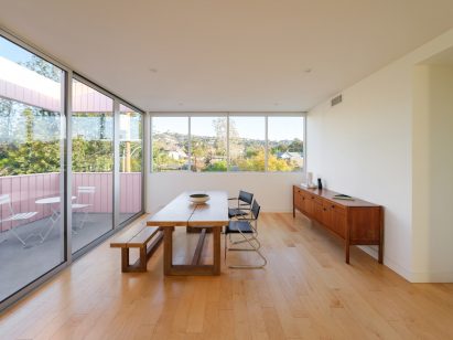 Dining room with wooden floors and sliding glass doors leading to a terrace with pink walls