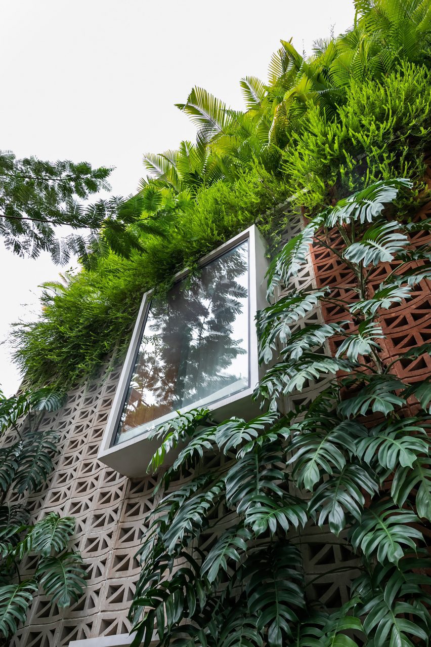 Perforated cement block facade covered in plants with an oriel window