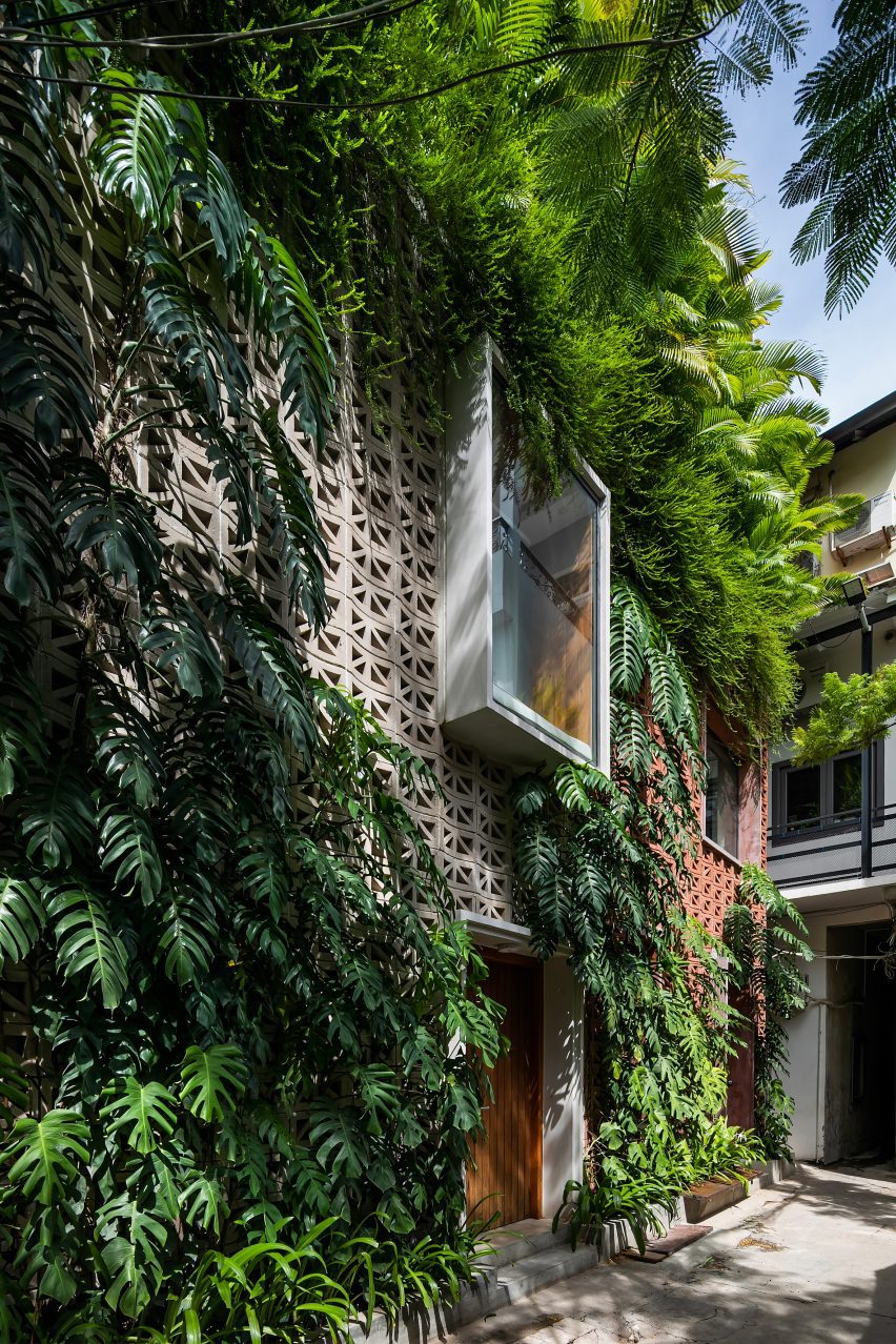 Perforated cement block facade covered in plants with an oriel window