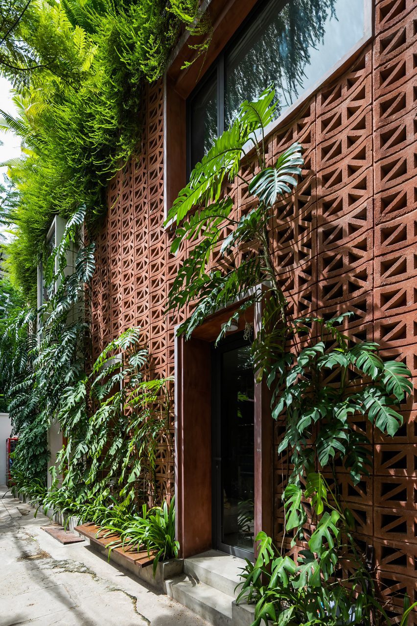 Red perforated cement block facade covered in plants